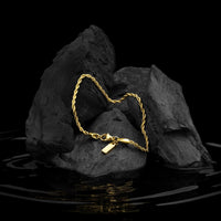 Gold bracelet on a rock with water reflection