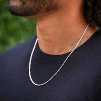 Man wearing a silver chain necklace against a blurred green background