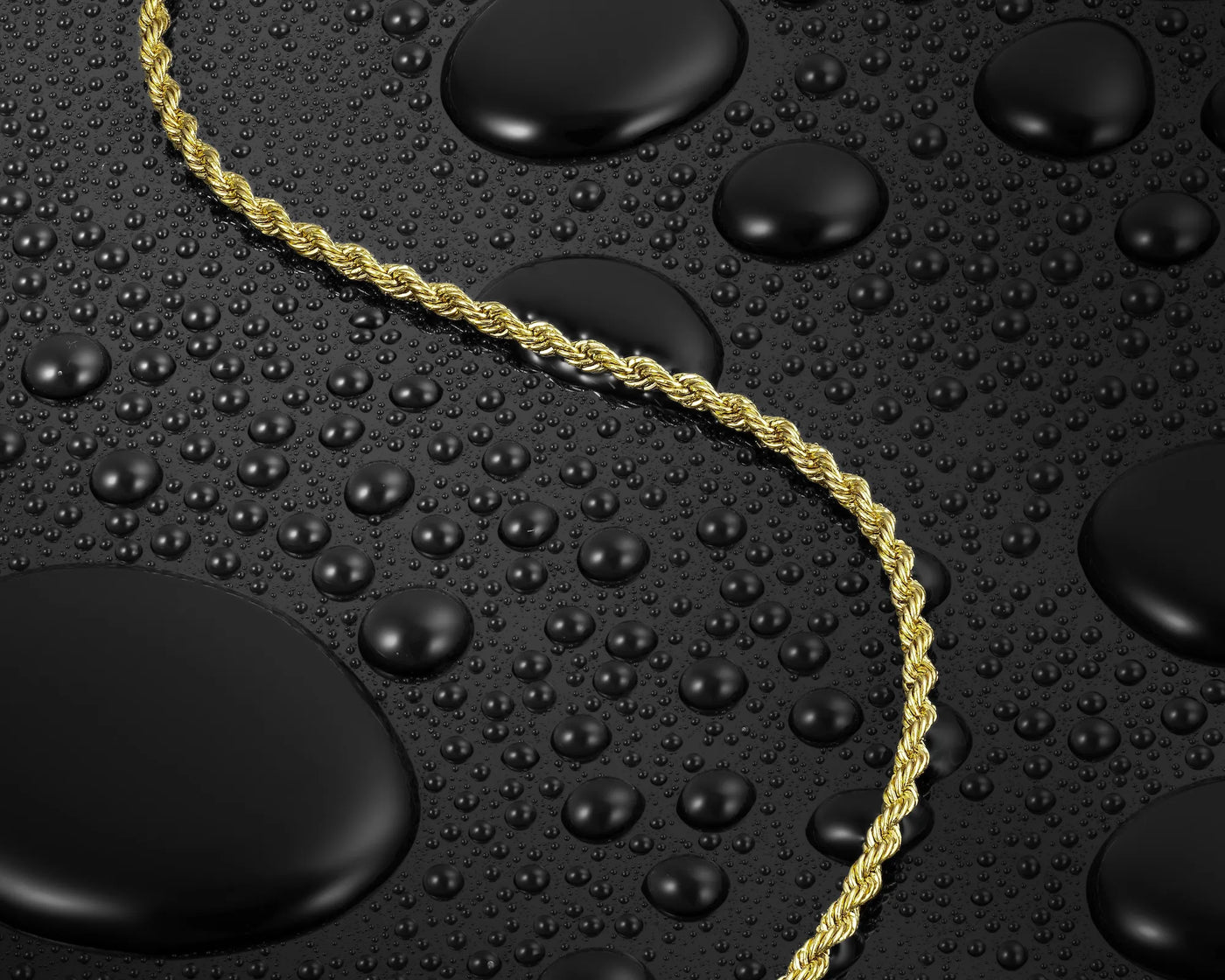 Gold rope chain on a black surface with water droplets