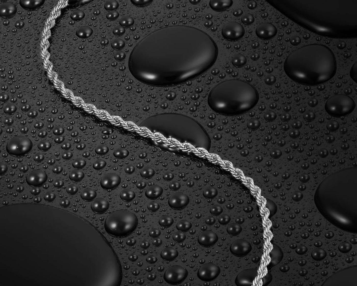Silver rope necklace on a textured black surface with water droplets