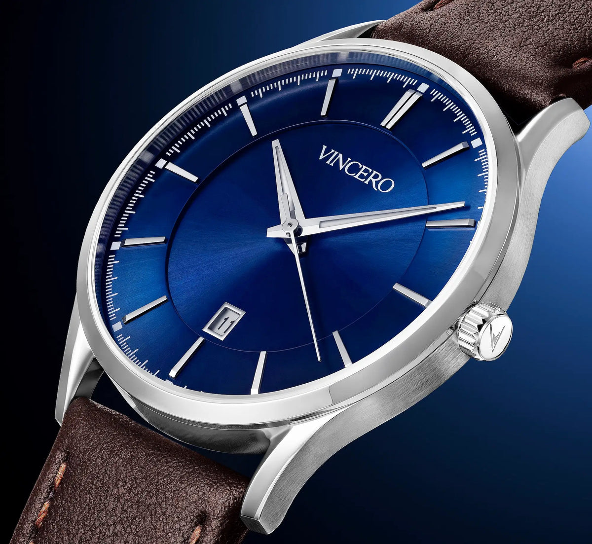 A close-up of a VINCERO wristwatch with a blue sunburst dial, silver stainless steel case, and a brown leather strap against a dark blue gradient background.