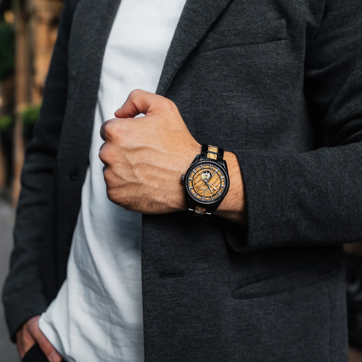 Person wearing a watch with a detailed face, dressed in a dark coat.