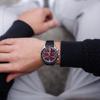 Person wearing a black wristwatch with a red face on a blurred background
