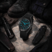 Black watch with blue digital display on a map with tactical gear around