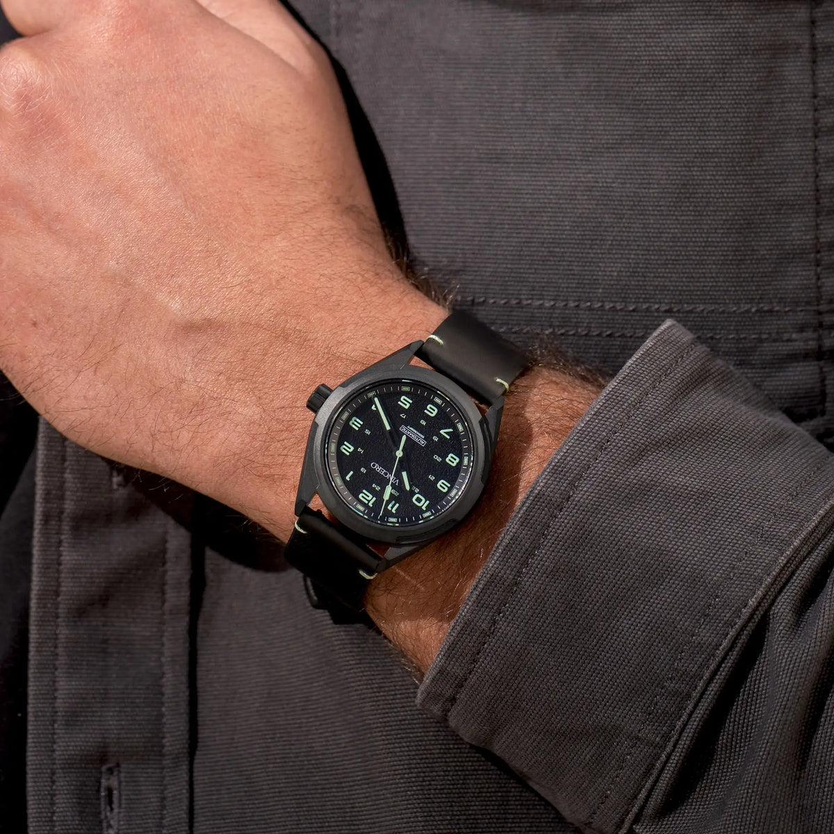 Black wristwatch on a person's wrist with a dark shirt background