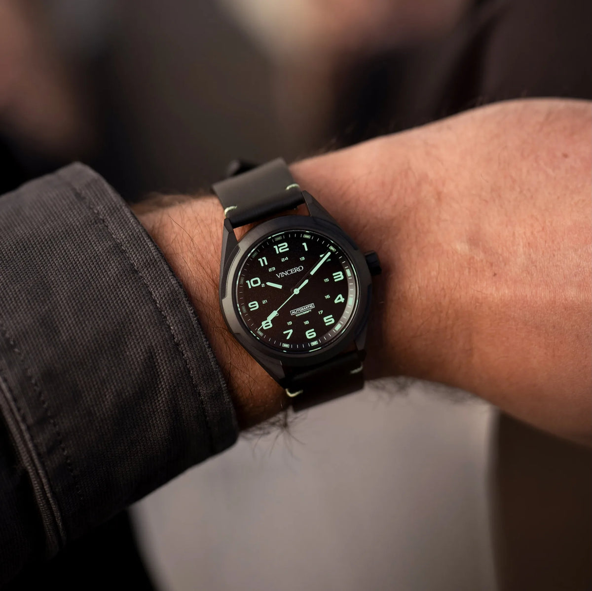 Black wristwatch with leather strap on a person's wrist, blurred background