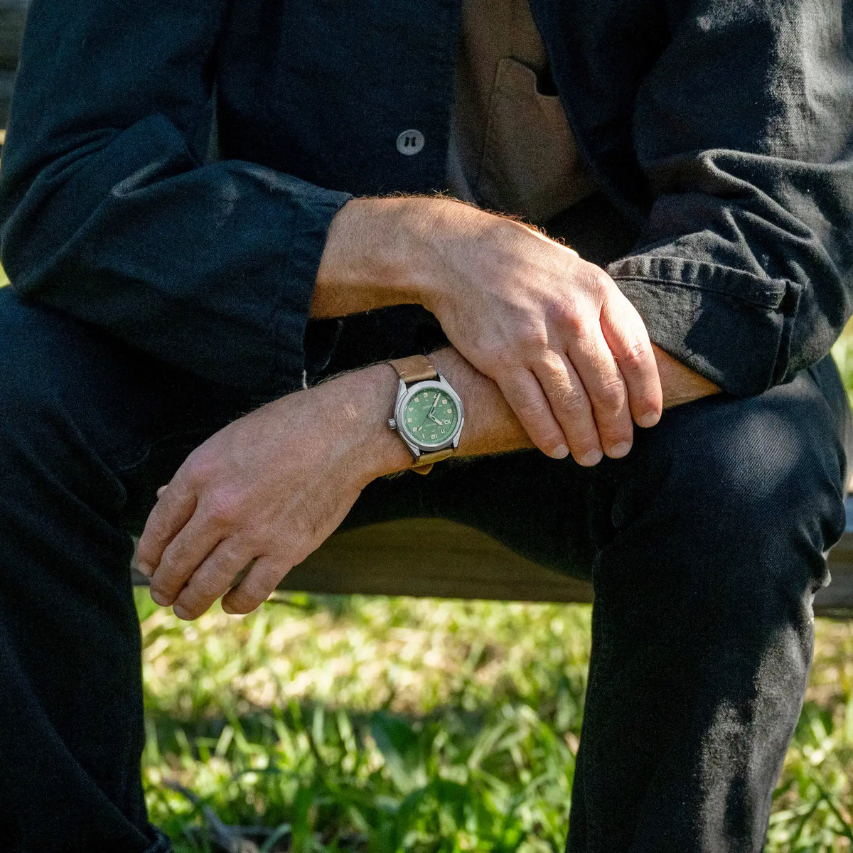 A silver-toned titanium watch with a green dial and a tan leather strap on wrist