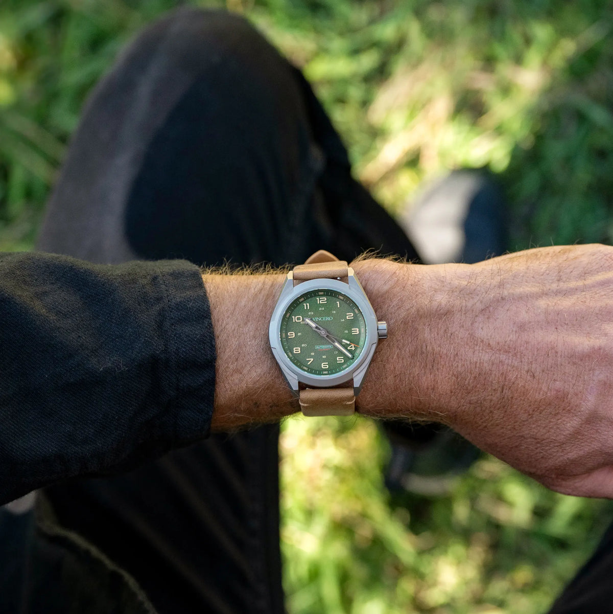 A silver-toned titanium watch with a green dial and a tan leather strap.