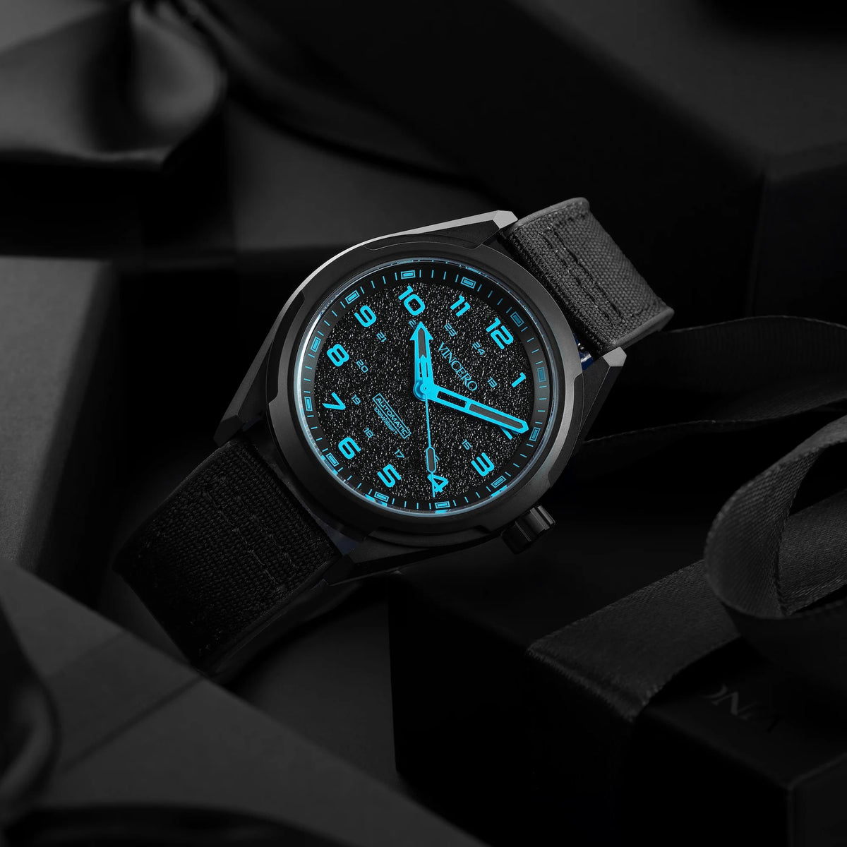 Black wristwatch with glowing blue face on a dark background