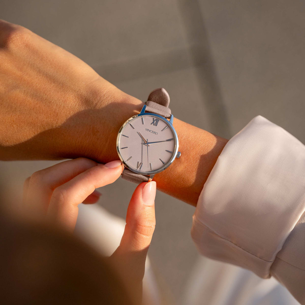 Person adjusting a watch on another person's wrist with a neutral background
