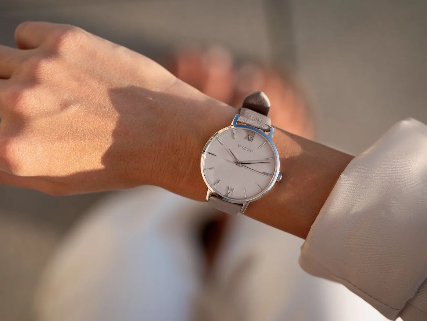 Person wearing a silver watch with a brown leather strap on a blurred background
