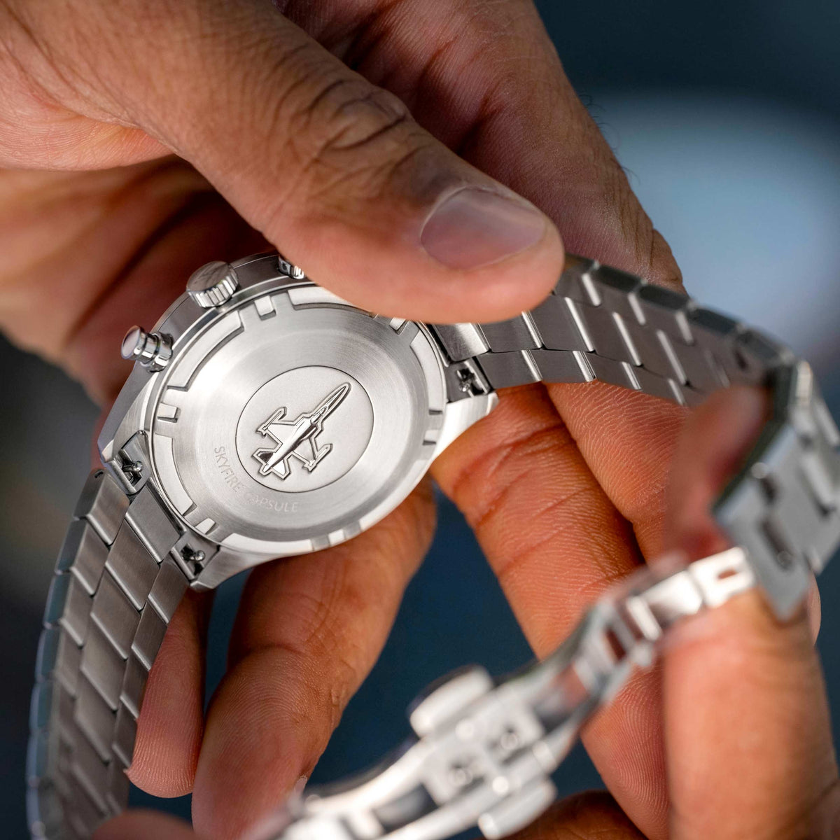 Close-up of a hand adjusting a silver watch with a visible brand logo.