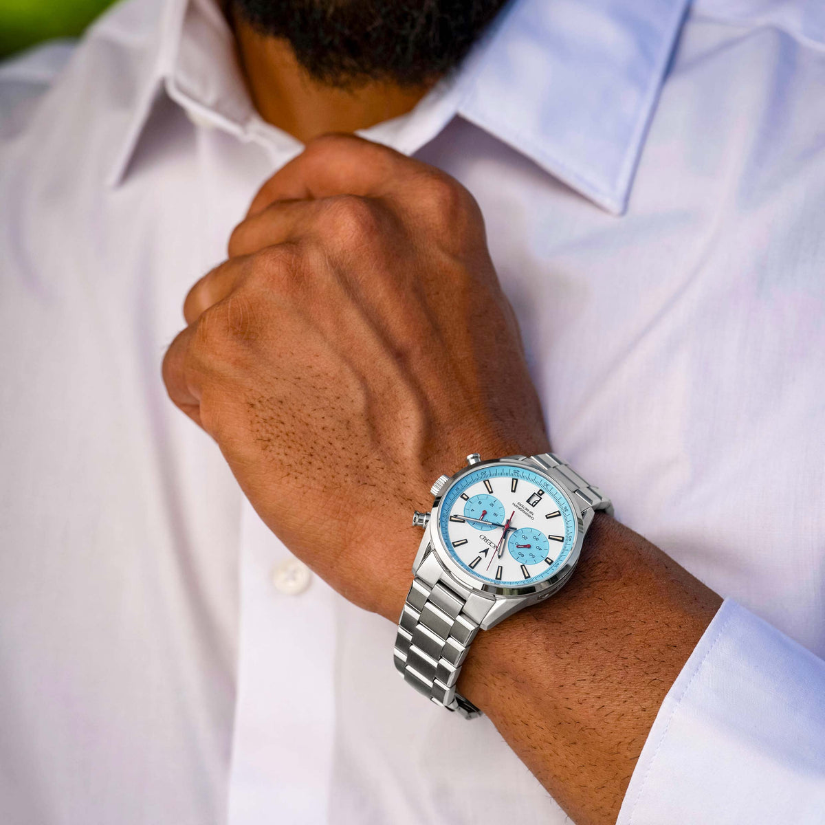 Person wearing a silver watch with a blue face on a white shirt background