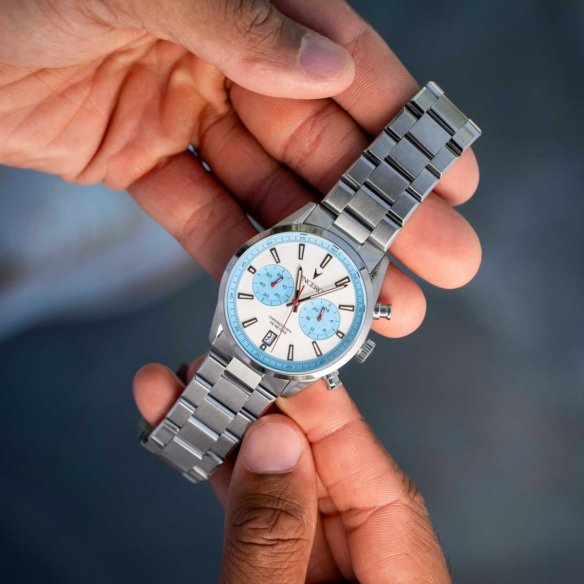 Silver watch with a blue face held in a hand against a blurred background
