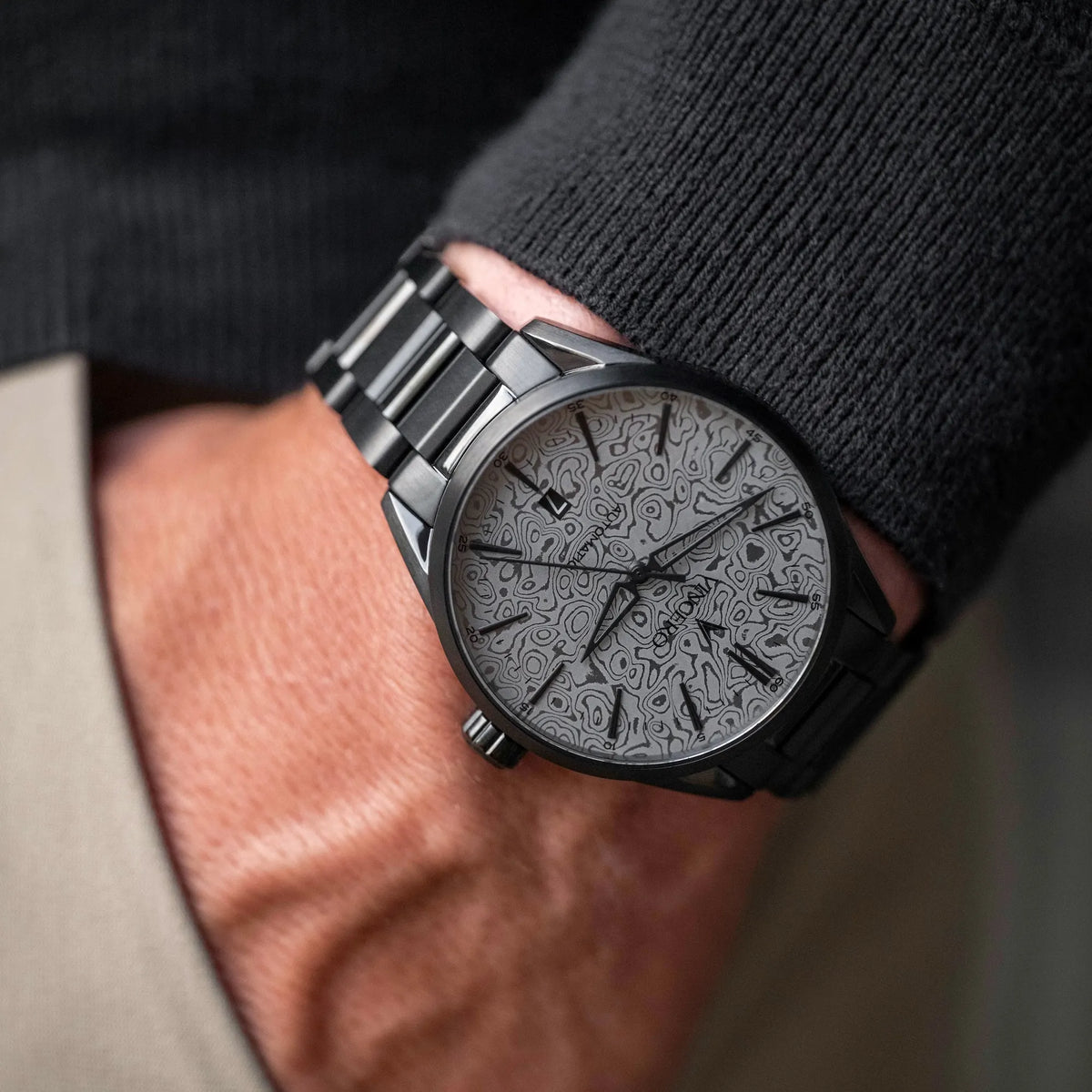 Black wristwatch with intricate design on a person's wrist