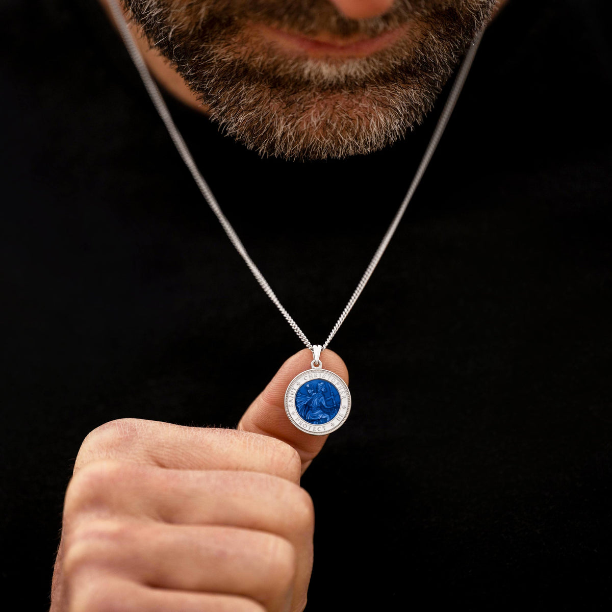 Man holding a silver necklace with a blue pendant against a black background