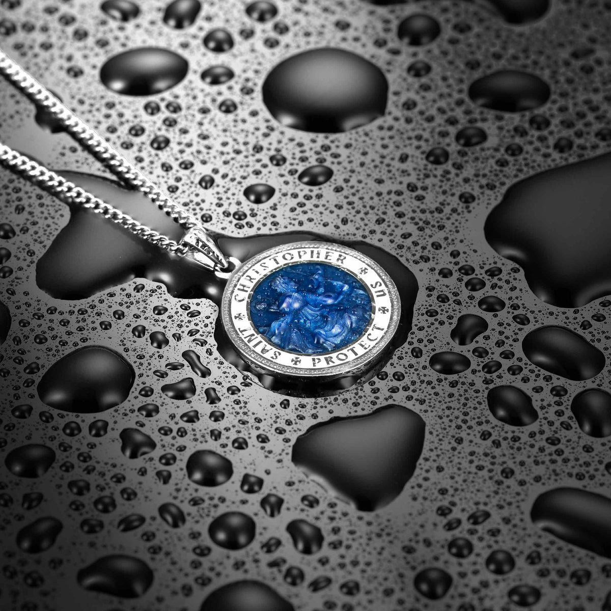 Silver necklace with a blue pendant on a textured black surface with water droplets.
