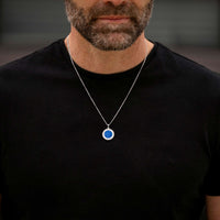 Man wearing a black shirt with a necklace featuring a blue pendant.