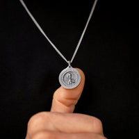 Silver necklace with a pendant held by a finger against a black background
