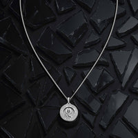 Silver necklace with a round pendant on a black textured background