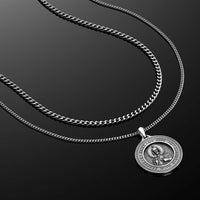 Silver chain necklace with a round pendant on a black background