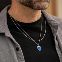 Man wearing a black shirt with a silver necklace featuring a blue pendant.