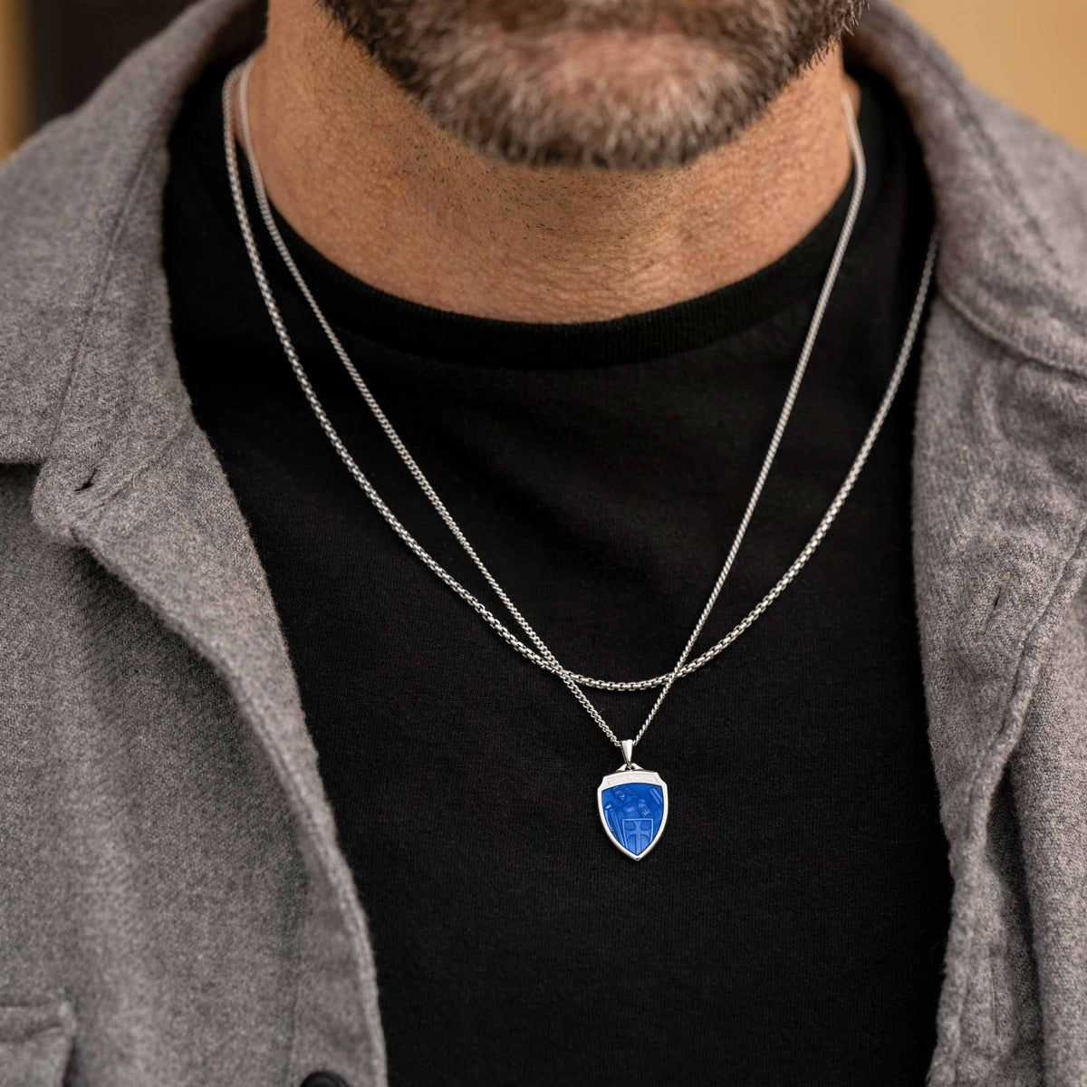 Person wearing a black shirt with a silver necklace featuring a blue pendant.