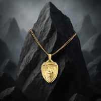 Gold necklace with a shield pendant on a dark rock with mountainous background