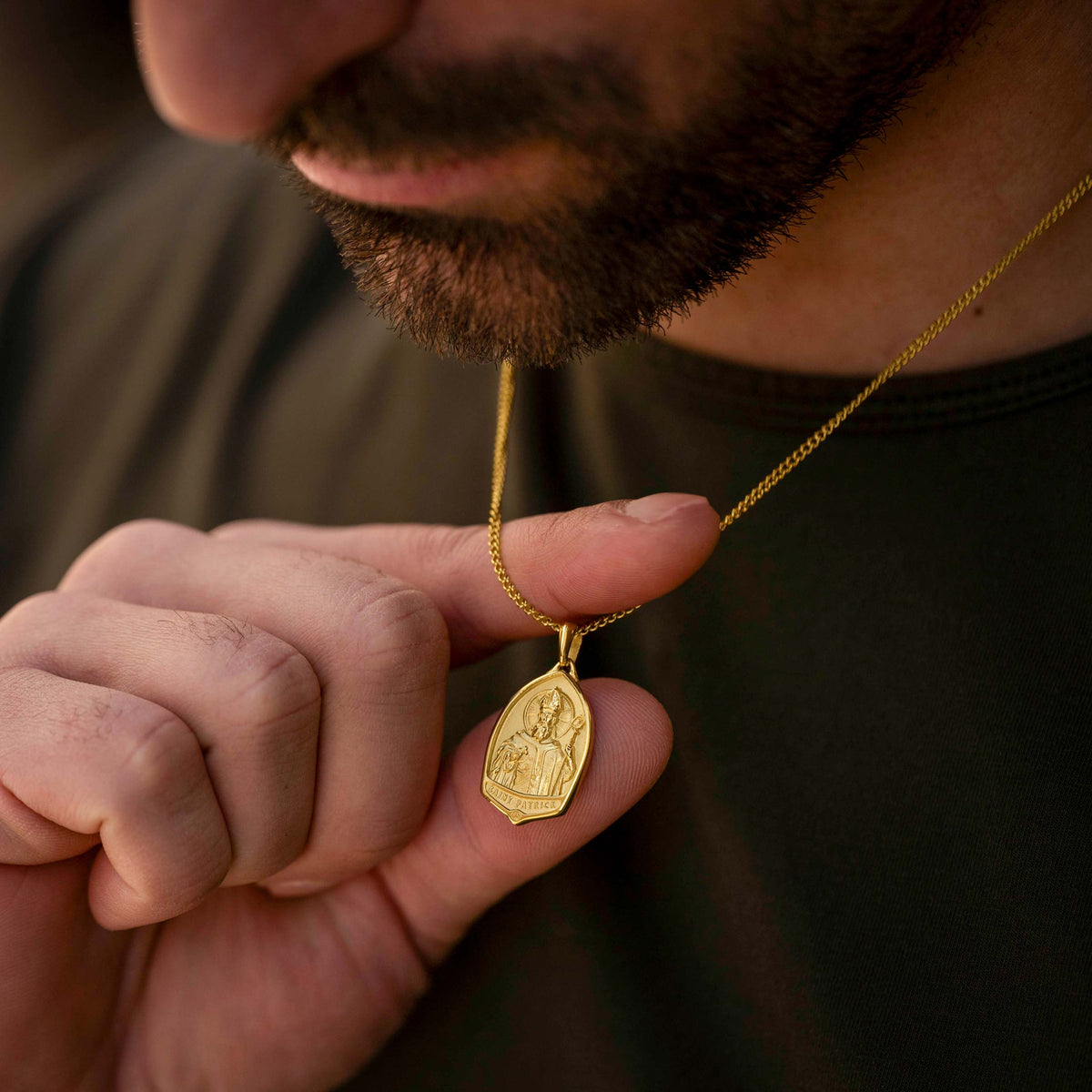 Man holding a gold necklace with a pendant
