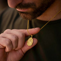 Man holding a gold necklace with a pendant