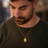 Man wearing a gold necklace with a pendant, looking down.