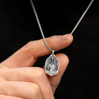 Silver pendant necklace held by a hand against a black background
