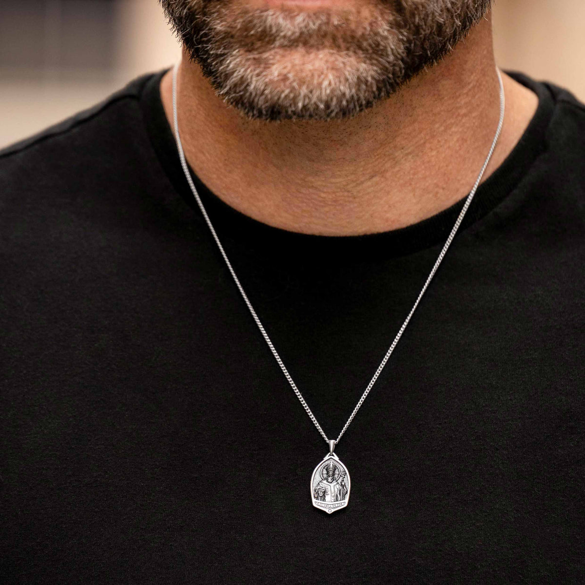 Man wearing a black shirt with a silver necklace featuring a pendant.