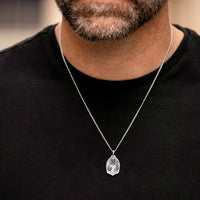Man wearing a black shirt with a silver necklace featuring a pendant.
