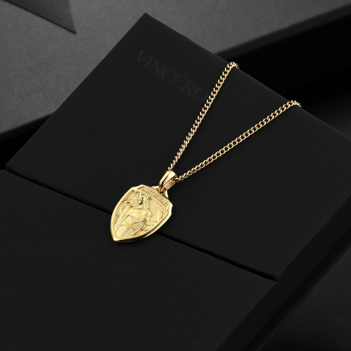 Gold necklace with a shield-shaped pendant on a black surface
