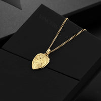 Gold necklace with a shield-shaped pendant on a black surface