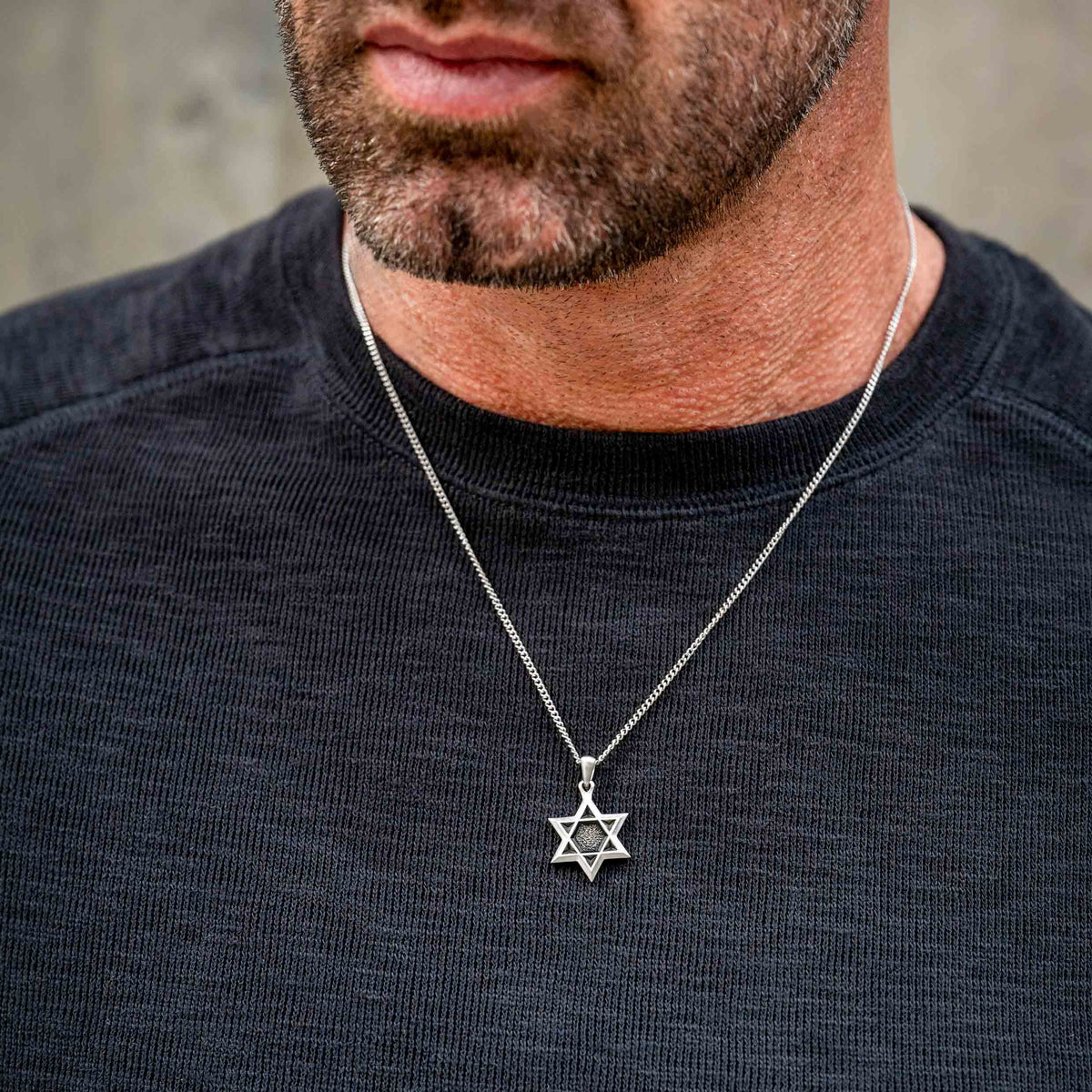 Man wearing silver chain necklace with silver Star of David pendant. 