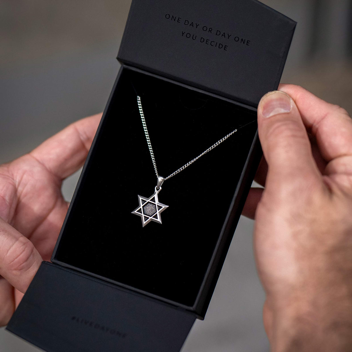 Man opening black box containing a silver chain necklace with silver Star of David pendant. 