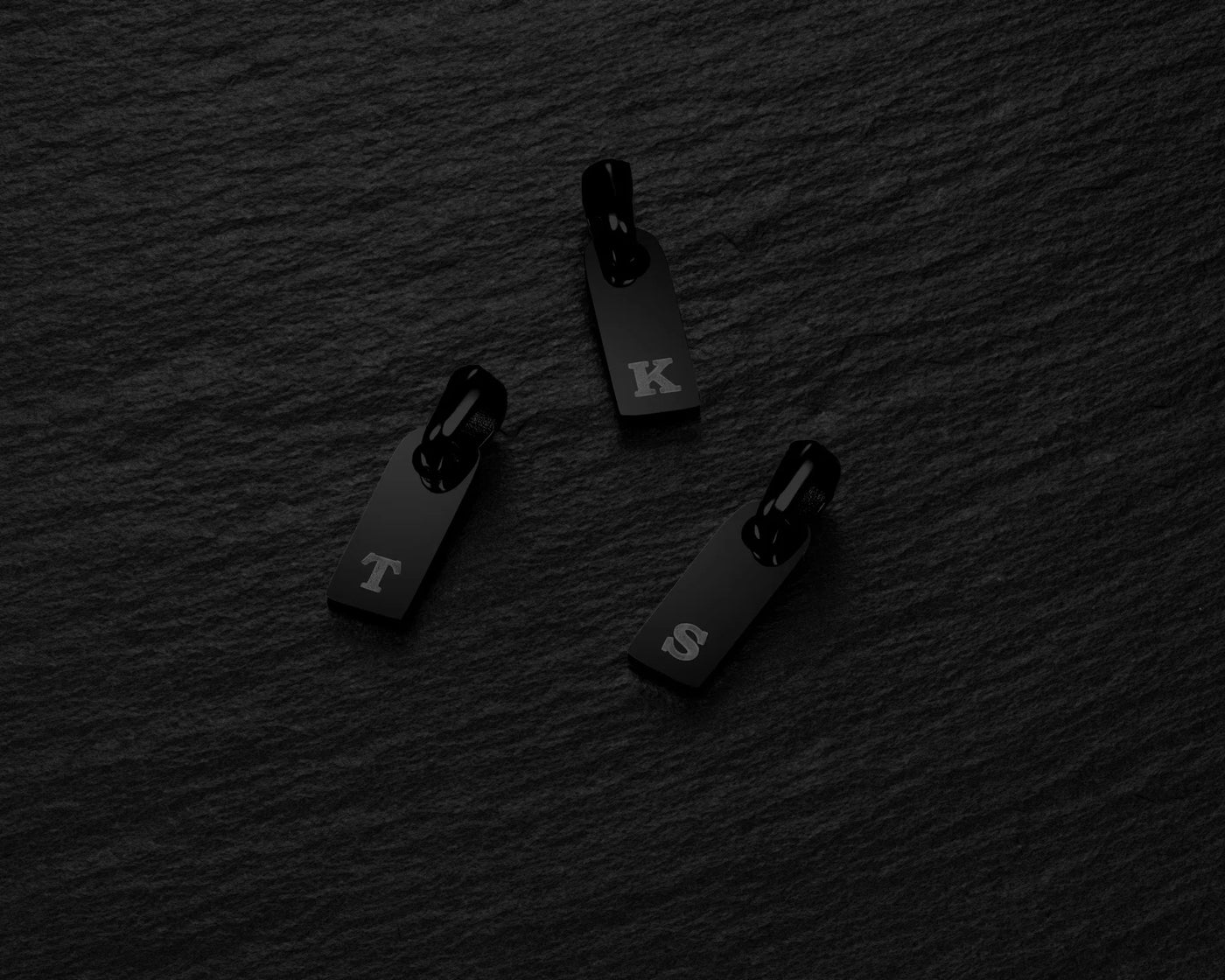 Black zipper pulls with 'T', 'K', and 'S' letters on a dark textured background