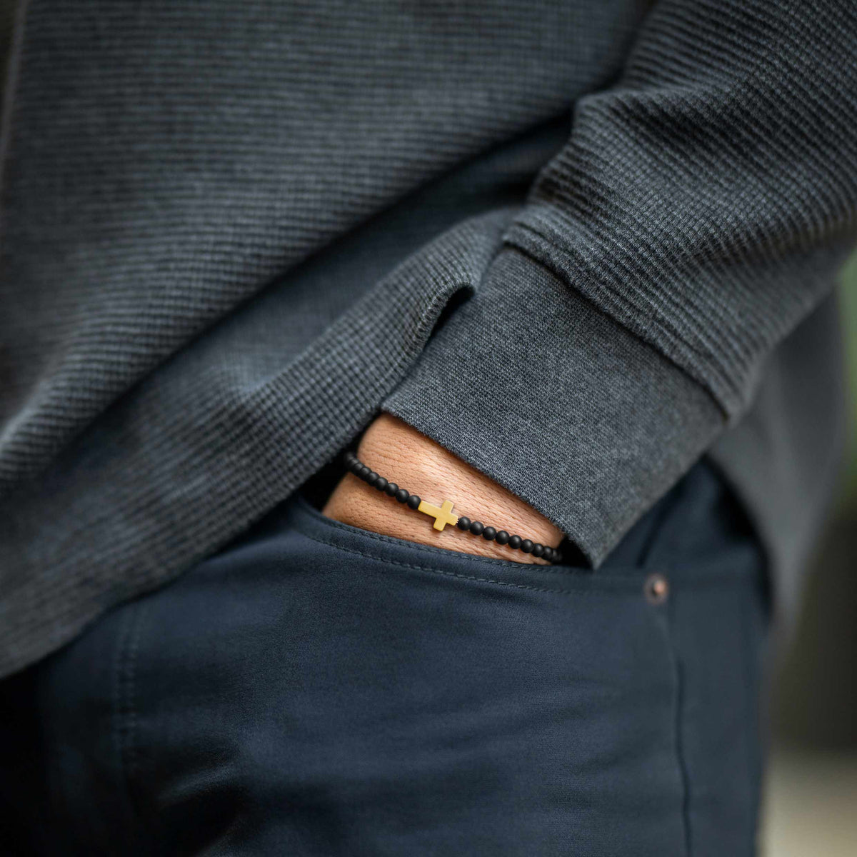 Person wearing a dark gray sweater with rolled-up sleeves, showing a bracelet on a blurred background.