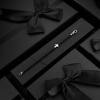Silver bracelet with a cross charm on a black gift box with a bow