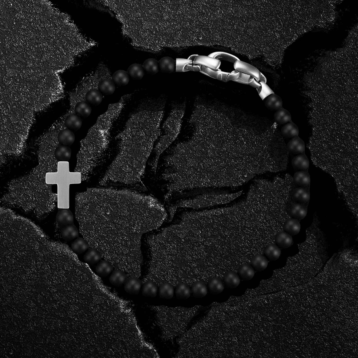 Black beaded bracelet with a silver clasp and cross charm on a textured black background