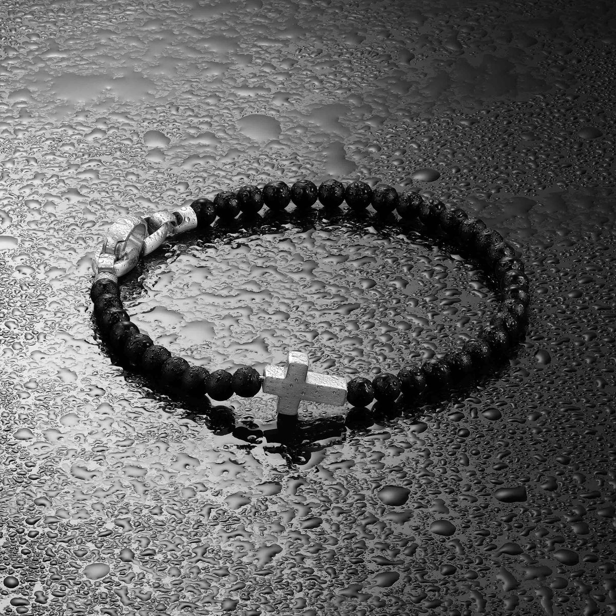 Black rosary with a cross on a wet surface