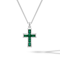 Silver cross pendant with green stones on a chain against a white background