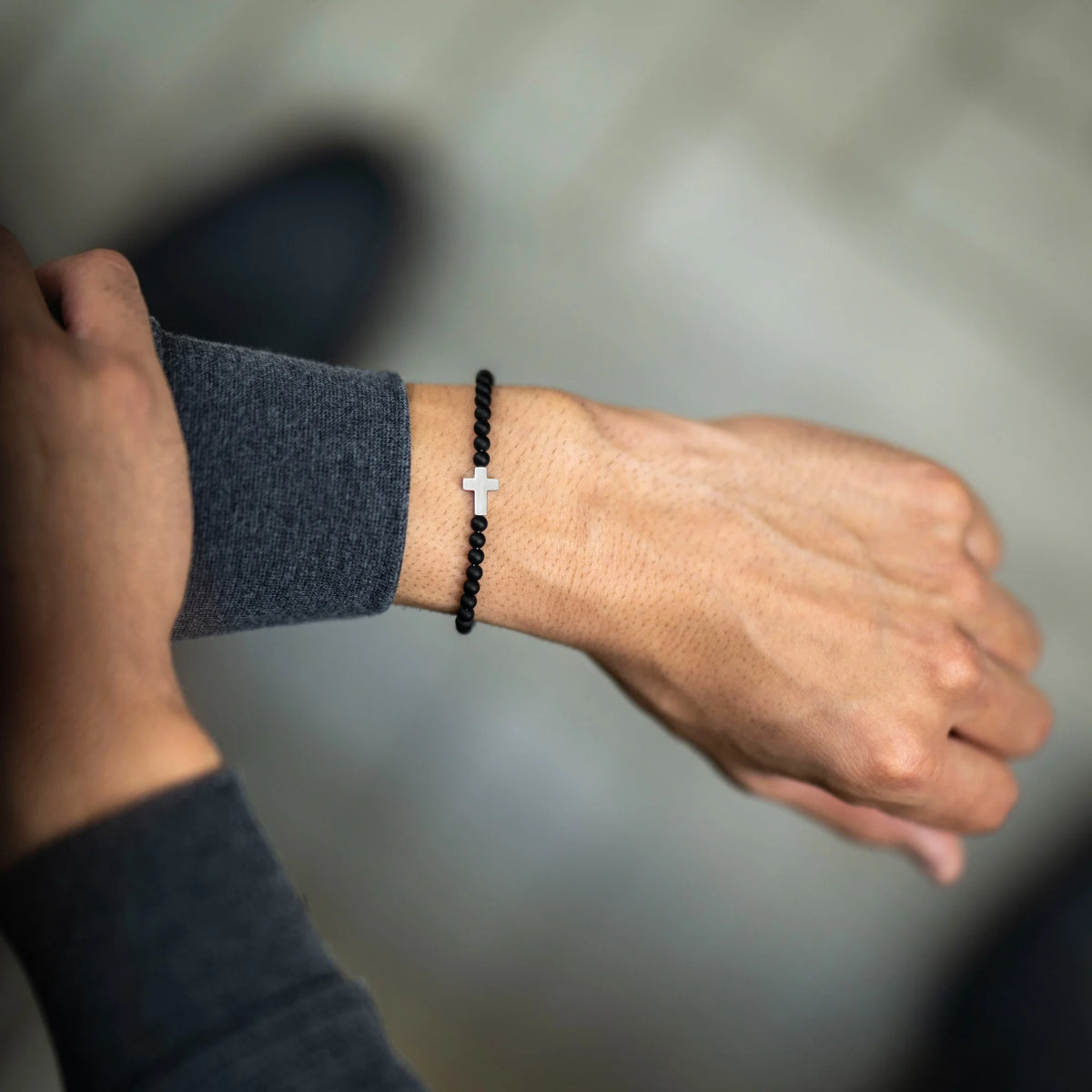 Person wearing a black beaded bracelet with a silver cross on a blurred background