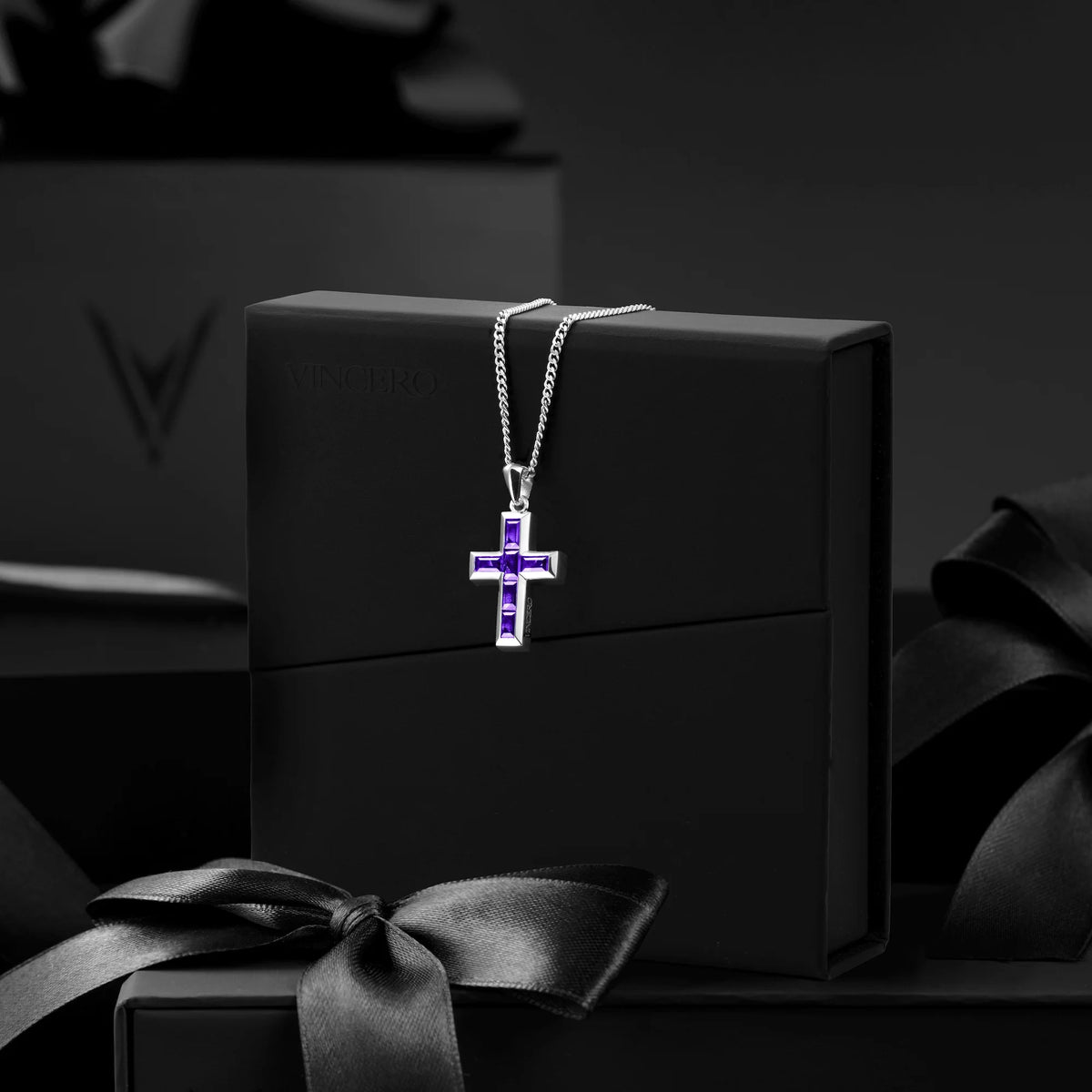 Silver cross necklace with purple stones on a black box with a ribbon