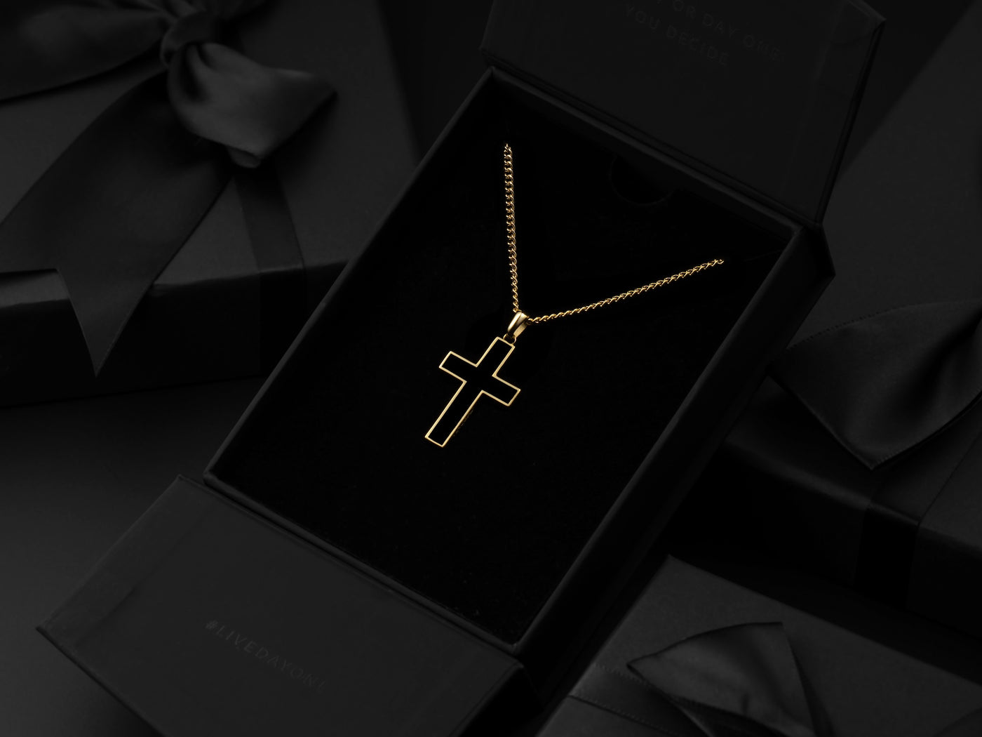 Gold chain necklace with a gold plated black stone cross, displayed in black packaging 