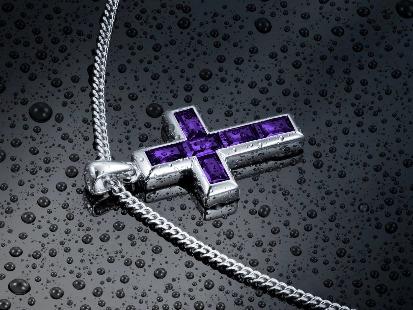 Silver cross pendant with purple gemstones on a textured dark surface