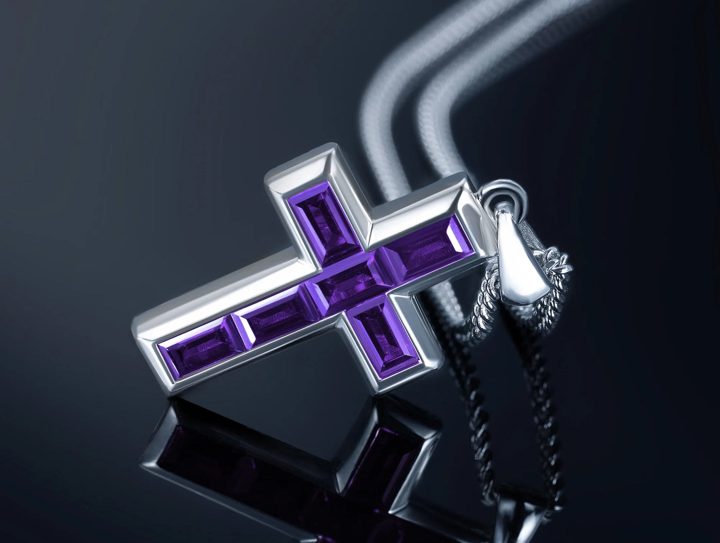 Silver cross pendant with purple gemstones on a reflective surface