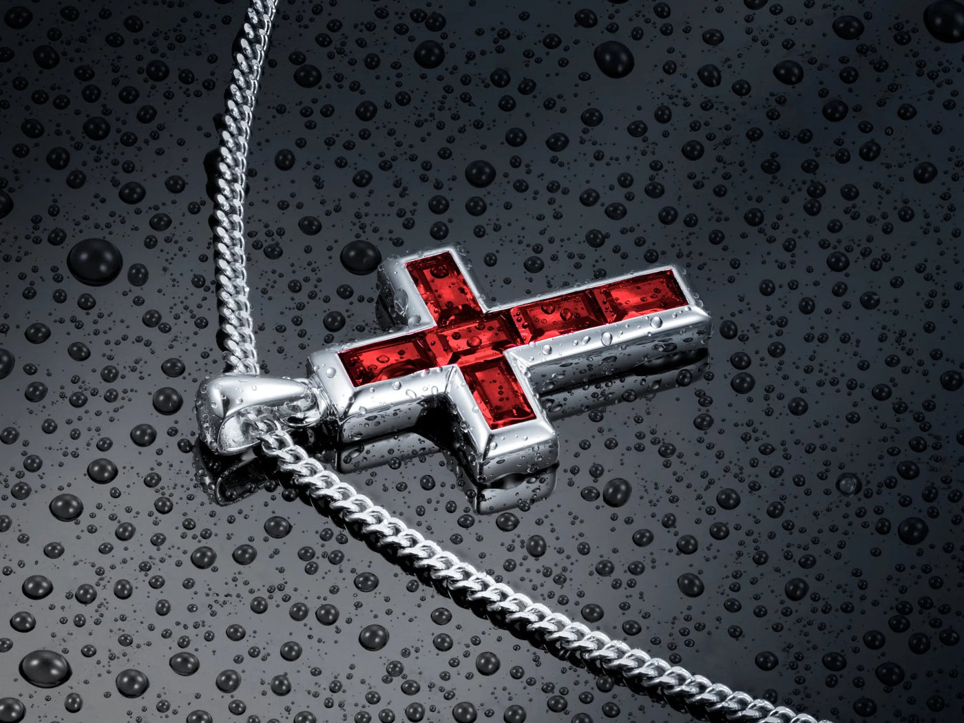 Silver cross pendant with red stones on a textured dark surface